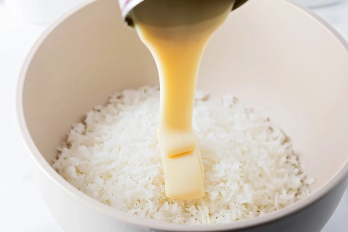 Adding condensed milk to the coconut for mounds bars in a grey bowl.