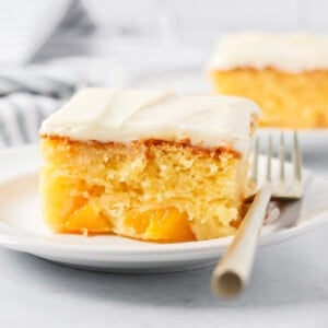 A slice of frosted peaches and cream cake on a white plate.