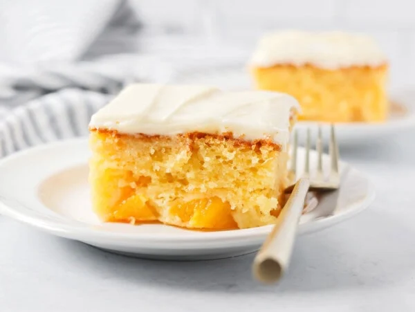 A slice of frosted peaches and cream cake on a white plate.