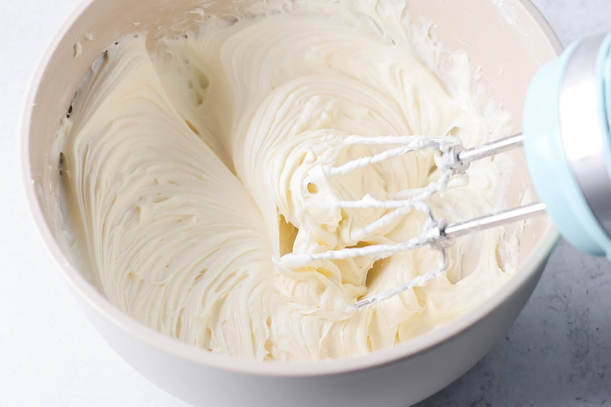 Whipping frosting in a bowl for peaches and cream cake.
