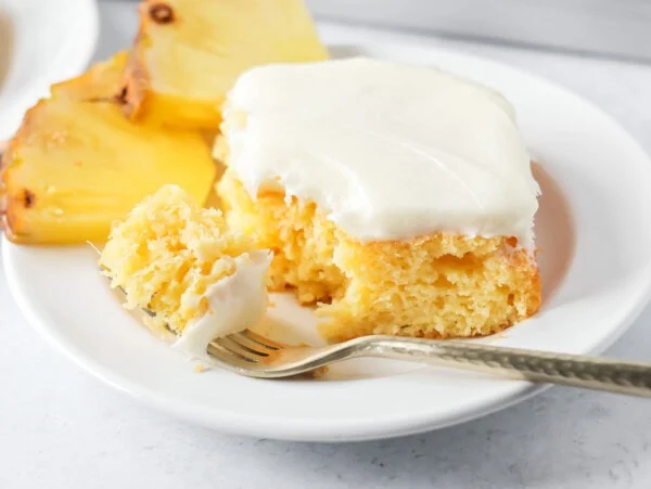 A slice of frosted easy pineapple cake with a bite missing.