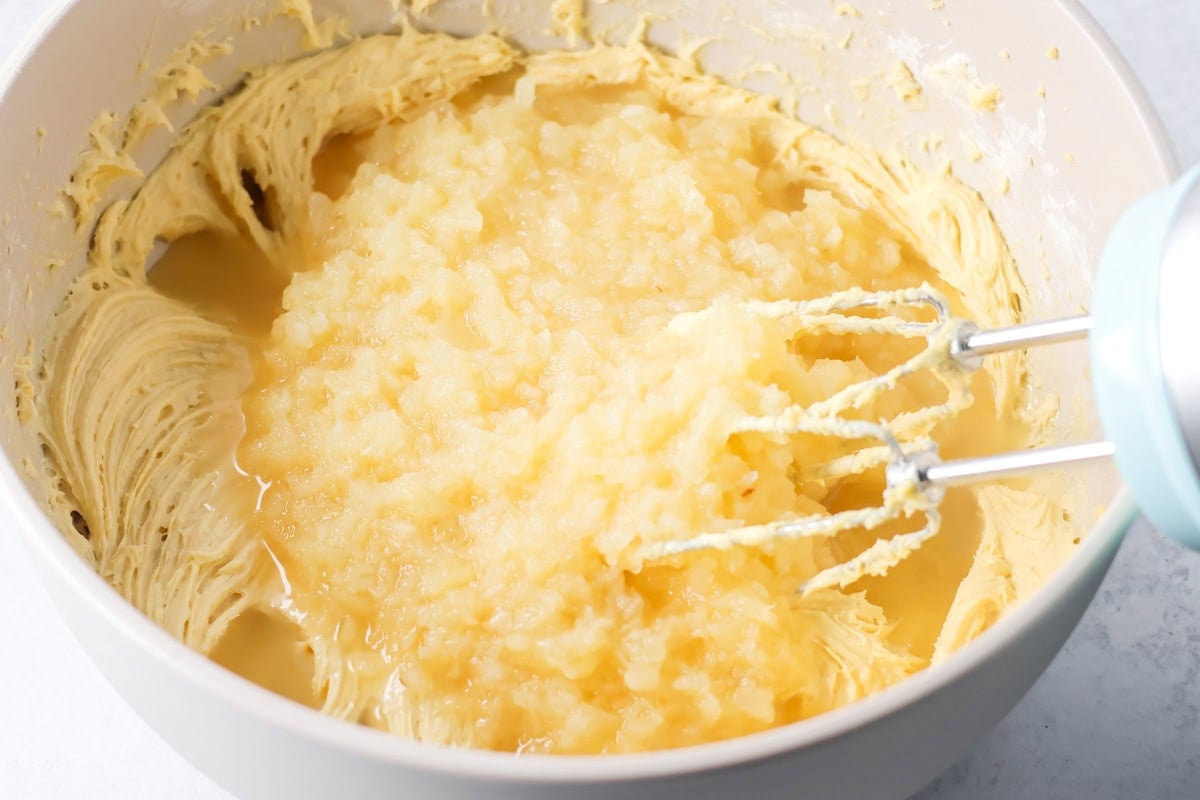 Adding pineapple to batter in a white bowl.