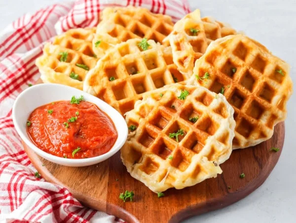 Six pizza waffles served on a wooden pizza peel with marinara.