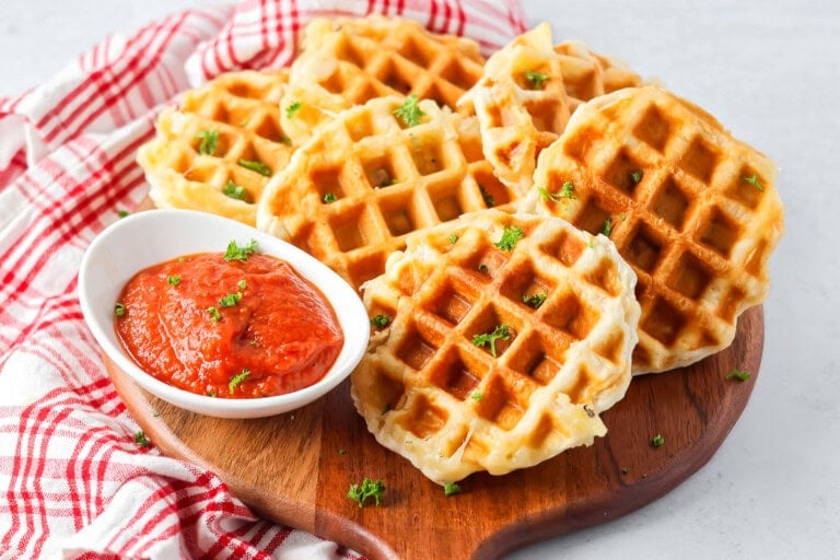 Six pizza waffles served on a wooden pizza peel with marinara.