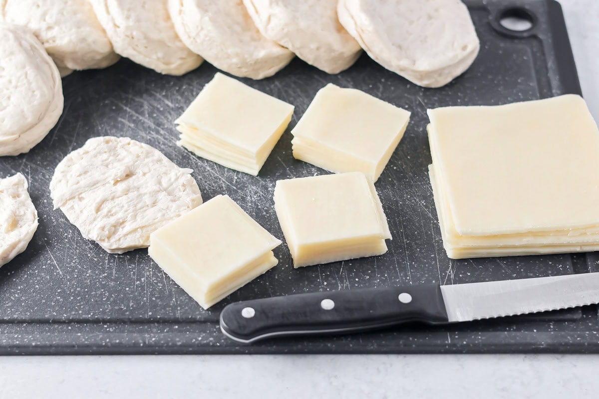 Biscuit dough and cheese slices on a cutting board.