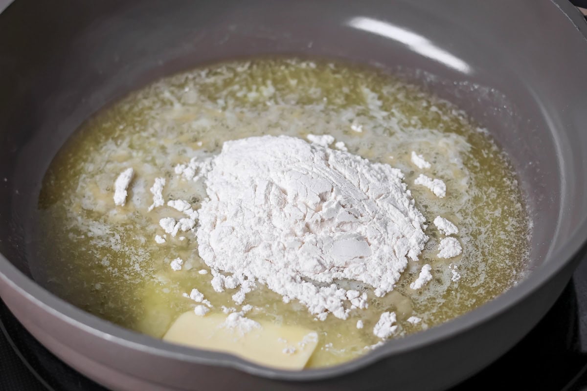 Adding flour to melted butter to make a roux.
