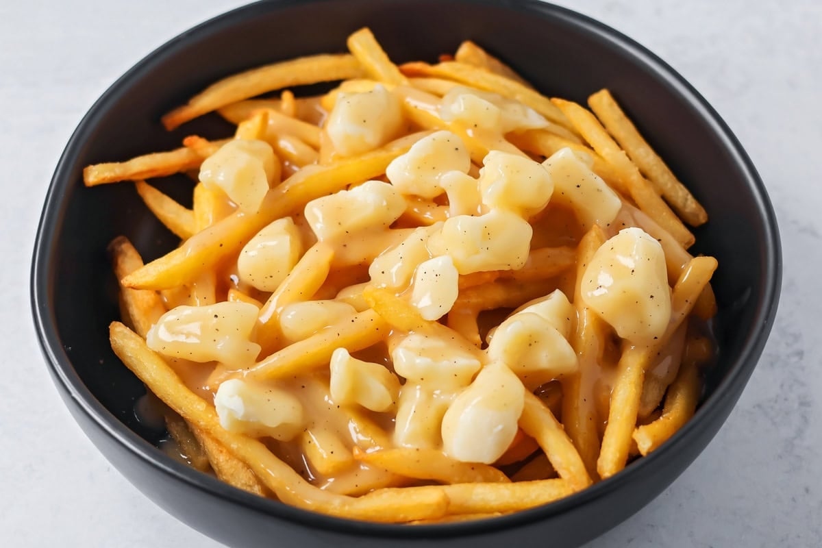 Adding cheese curds and gravy to a bowl of french fries for poutine recipe.
