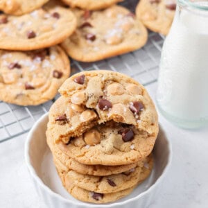 Salted Caramel chocolate chip cookies stacked on each other with cup of milk.