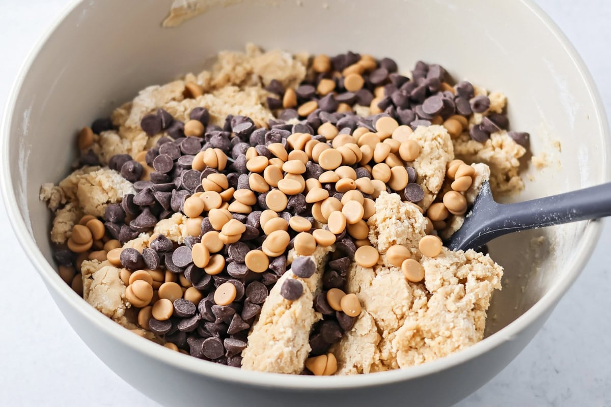 Chocolate and caramel chips on cookie dough in bowl.