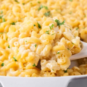 Scooping baked mac and cheese from a pan full.