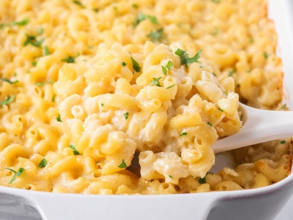 Scooping baked mac and cheese from a pan full.