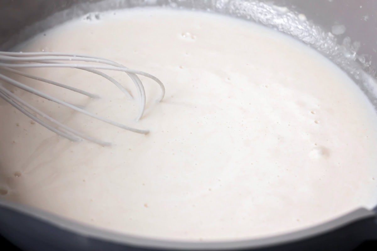 Whisking a white sauce in a pan for baked mac and cheese.