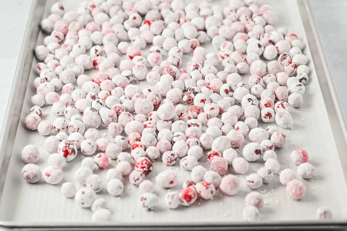 Candied cranberries covered in powdered sugar and spread on a baking sheet.