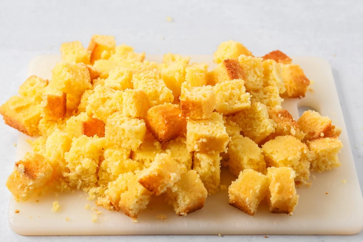 Cubed cornbread on a cutting board for making cornbread croutons recipe.
