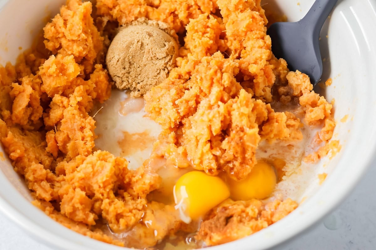 Adding eggs and brown sugar to crock pot sweet potato casserole filling.