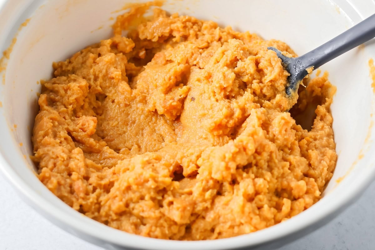 Mixing sweet potato casserole filling in a bowl.