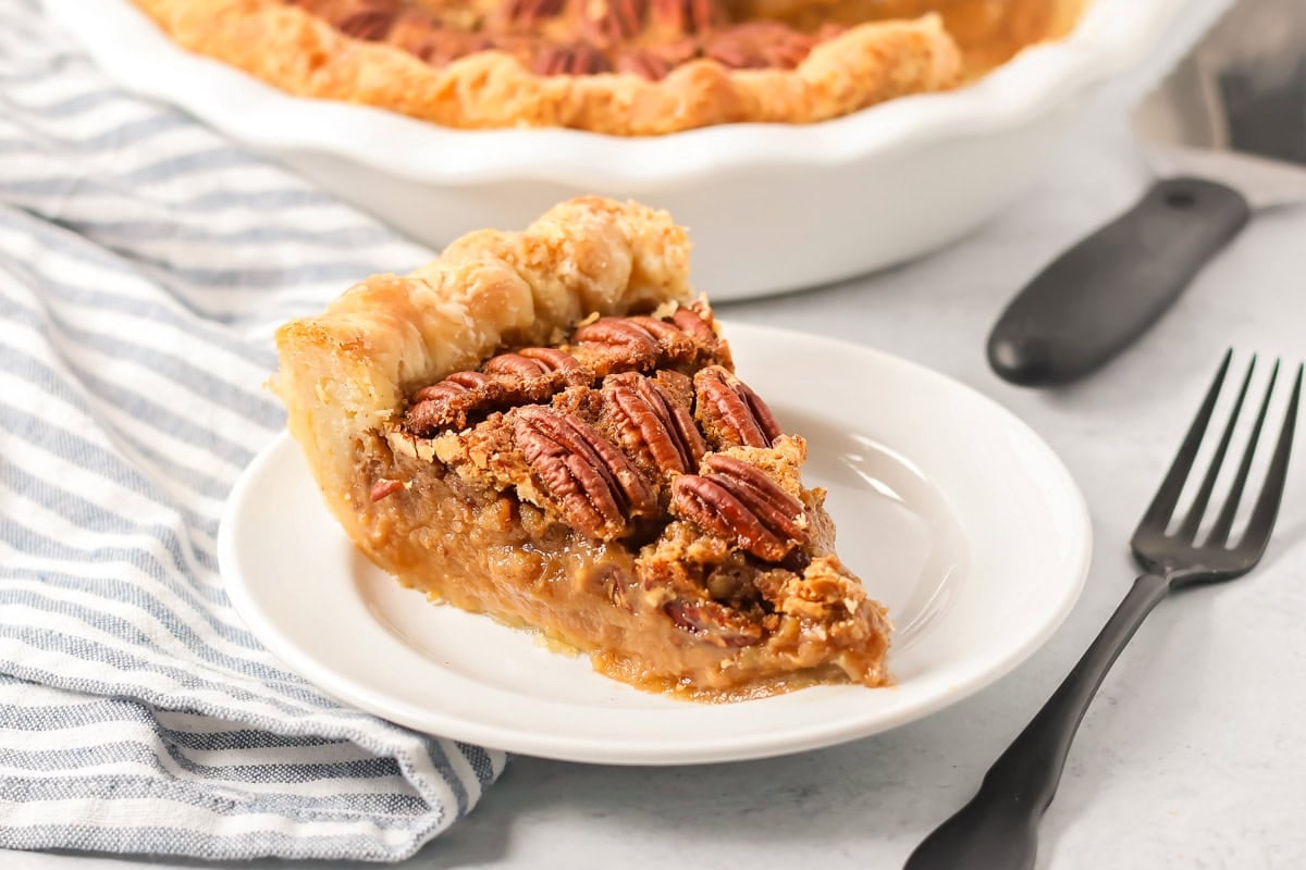 A slice of custard pecan pie on a white plate.