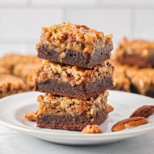 Three pecan pie brownies cut and stacked on a plate.