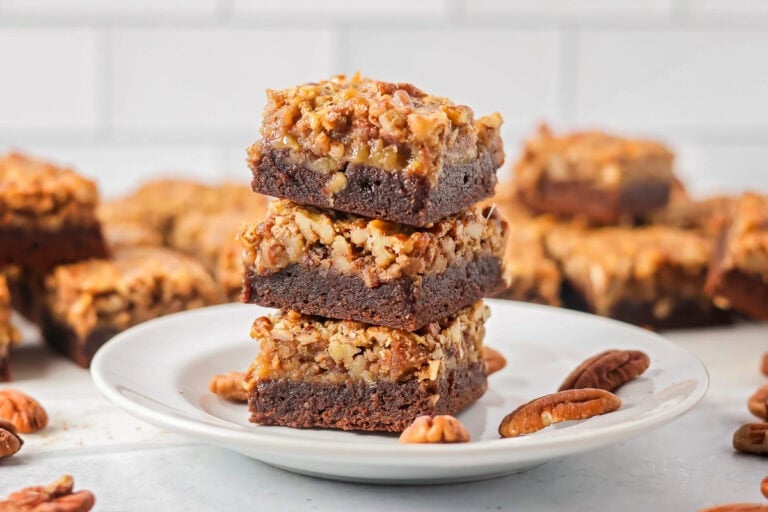 Three pecan pie brownies cut and stacked on a plate.