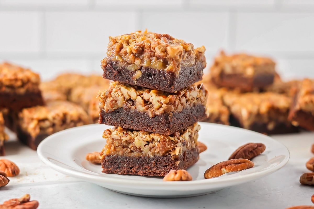 Three pecan pie brownies cut and stacked on a plate.