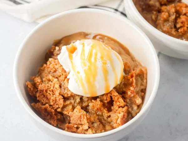 A serving of pecan pie dump cake topped with vanilla ice cream and caramel sauce.