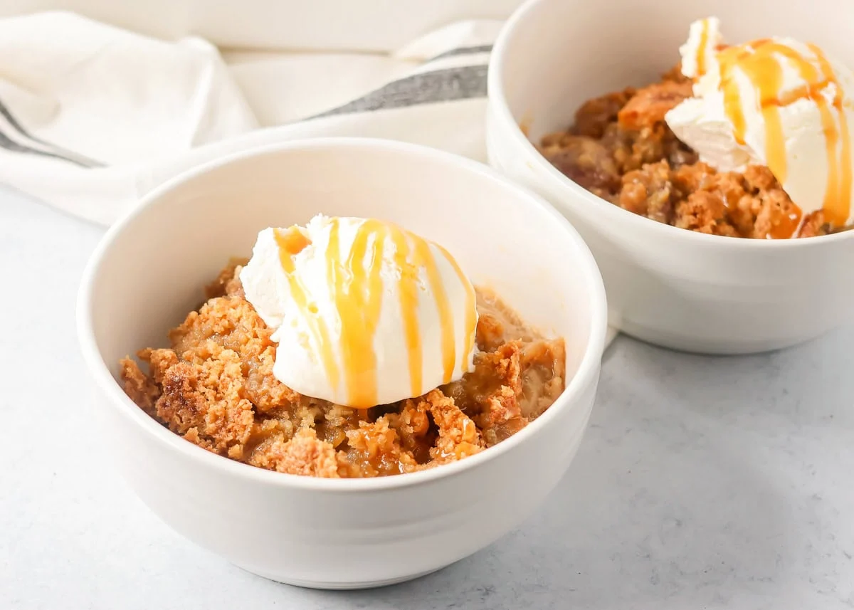 A bowl of pecan pie dump cake topped with vanilla ice cream and drizzled with caramel.