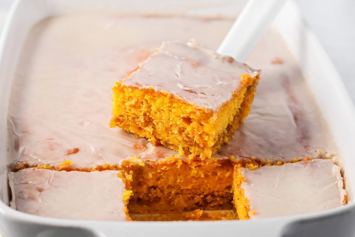 Pulling a slice of pumpkin honey bun cake from a baking pan.