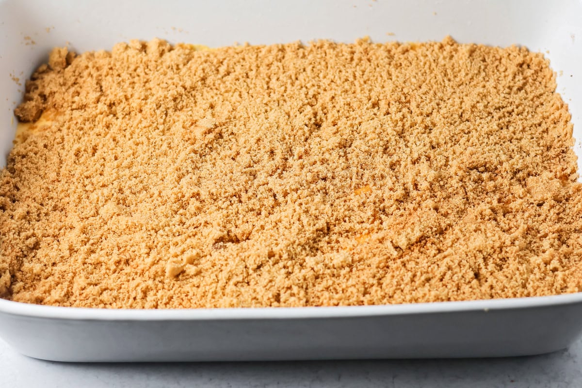 Sprinkling brown sugar mixture over pumpkin honey bun batter in a white baking dish.