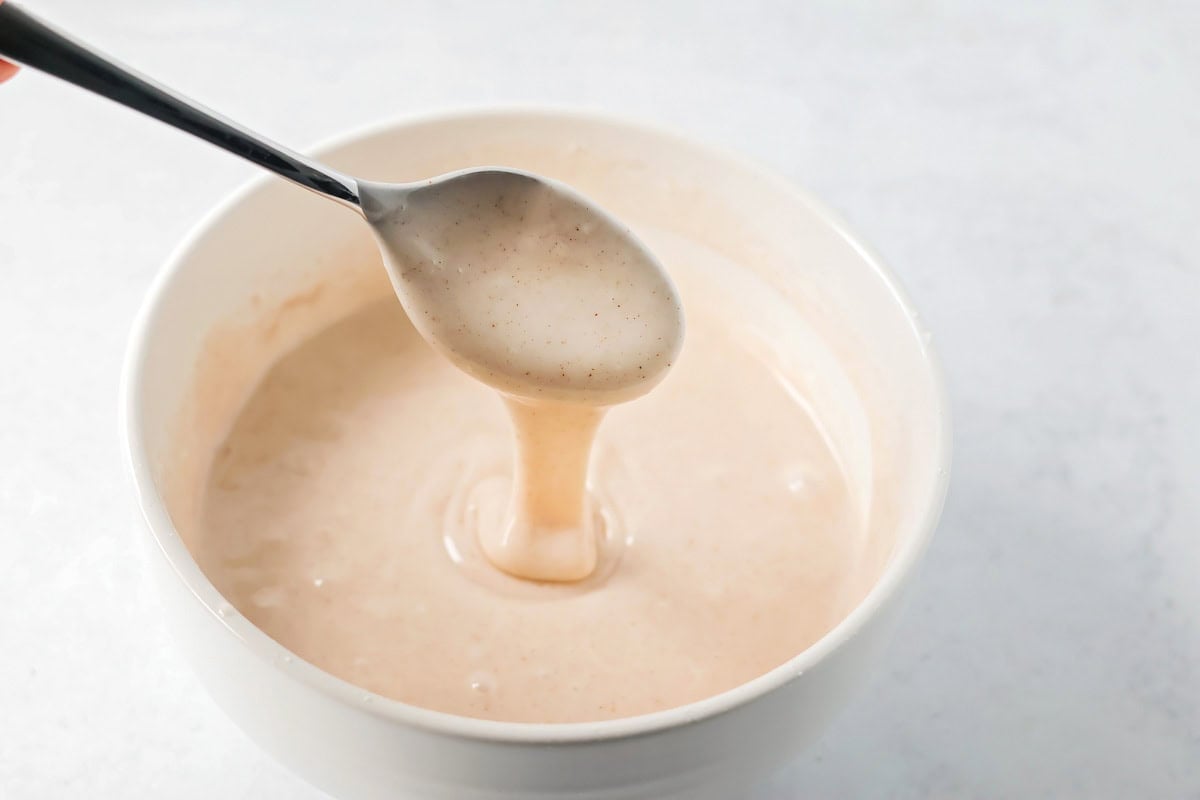 Spooning glaze for pumpkin honey bun cake in a white bowl.