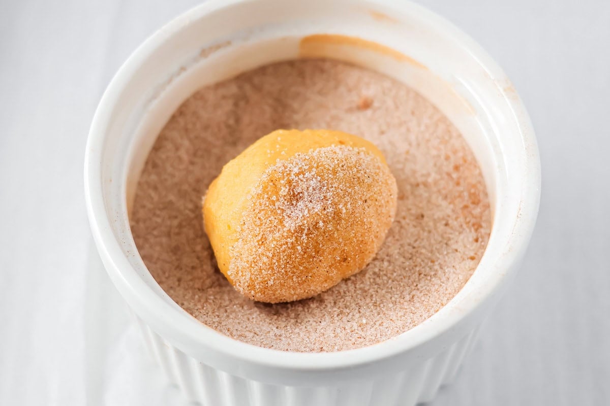Rolling pumpkin snickerdoodle dough ball in cinnamon sugar mixture.