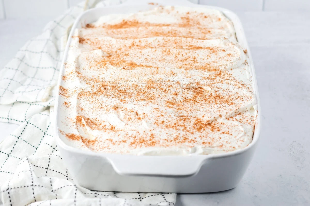 Spreading topping and cinnamon on a pumpkin tres leches cake.