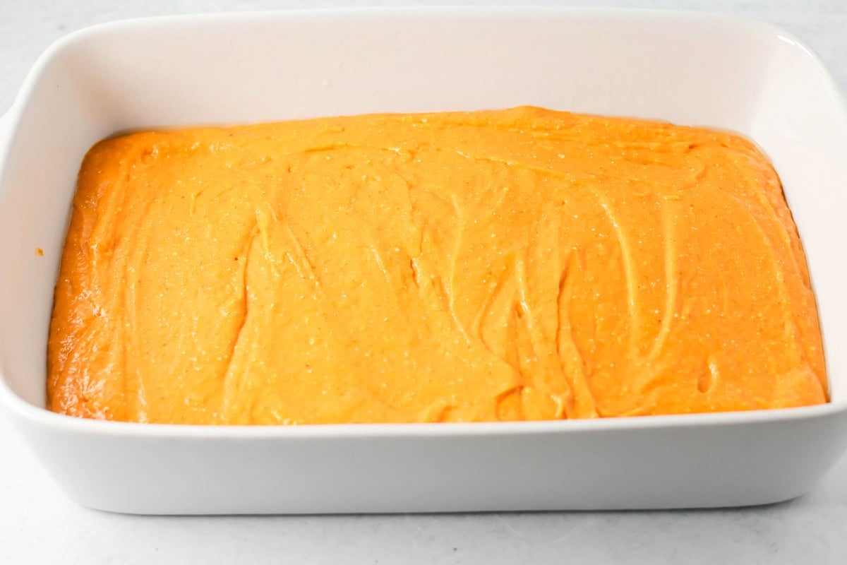 Spreading pumpkin tres leches batter in a baking dish.
