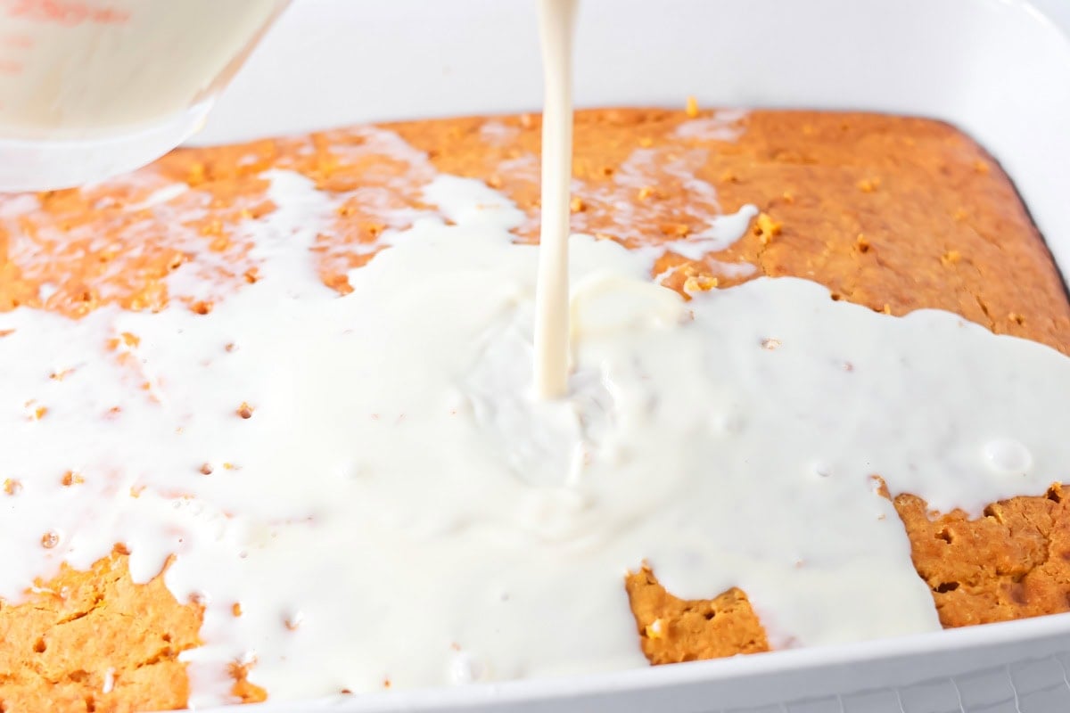 Pouring milk mixture on a pumpkin tres leches cake.