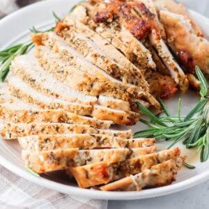 Sliced roasted turkey breast on a platter with fresh rosemary.