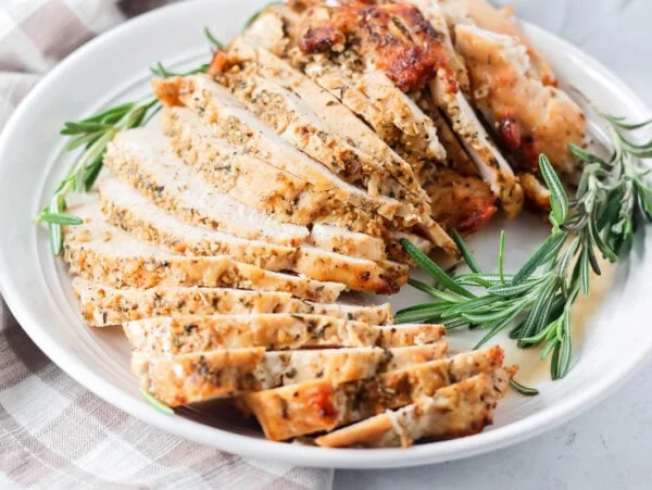 Sliced roasted turkey breast on a platter with fresh rosemary.