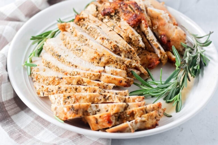 Sliced roasted turkey breast on a platter with fresh rosemary.