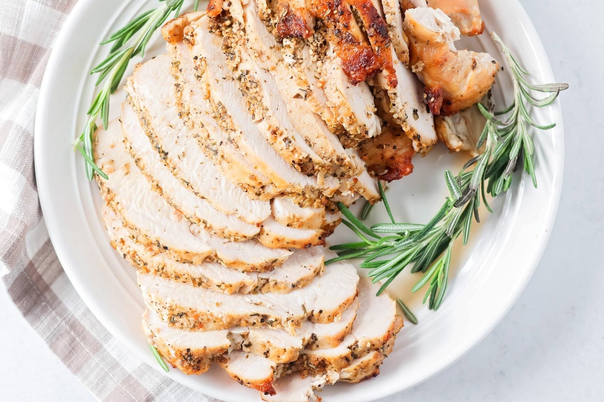 Sliced roasted turkey breast served on a white plate with rosemary.