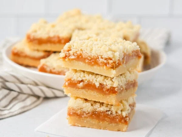 Three stacked salted caramel cookie bars on parchment paper.