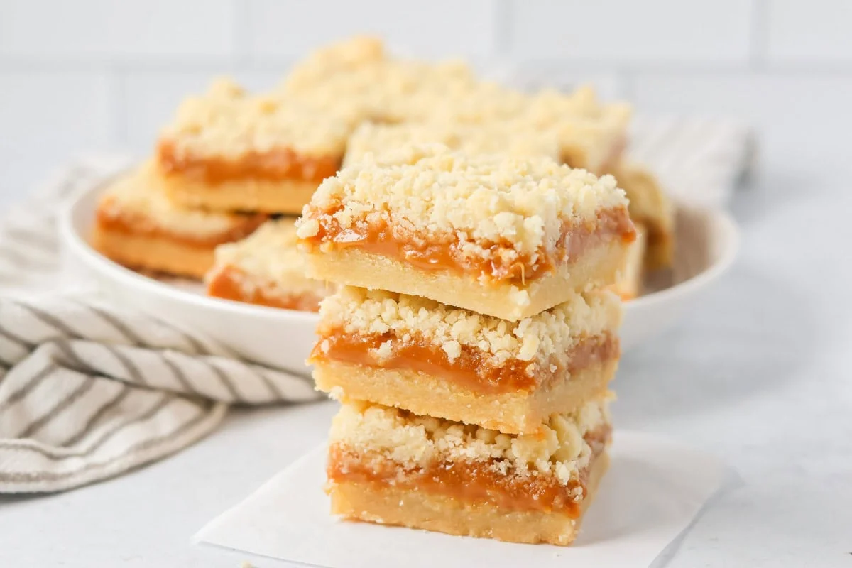 Three stacked salted caramel cookie bars on parchment paper.