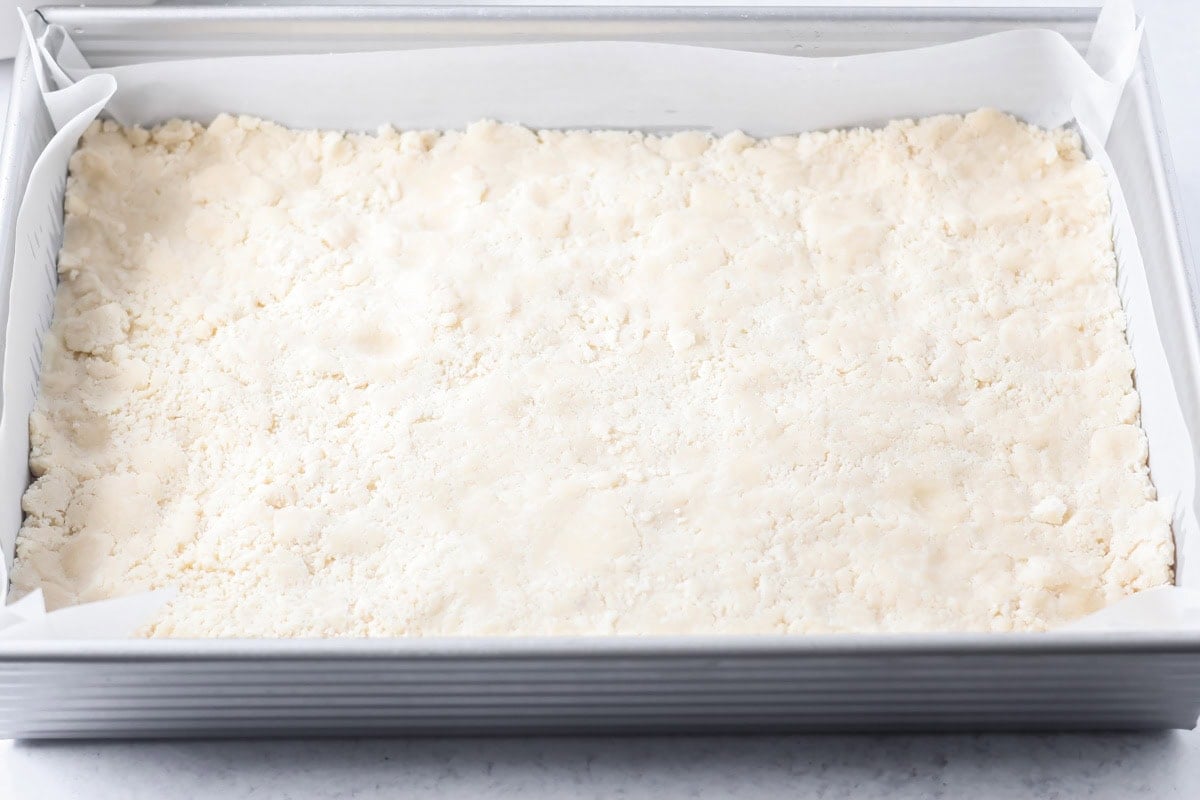 Pressing salted caramel cookie bars crust in a baking dish.