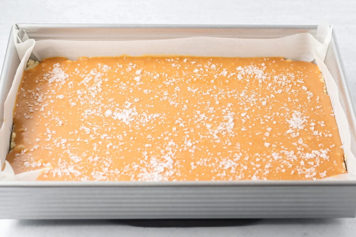 Salt spread on caramel layer for making salted caramel cookie bars.