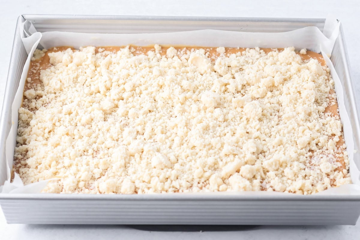 Crust sprinkled on salted caramel cookie bars in a baking pan.