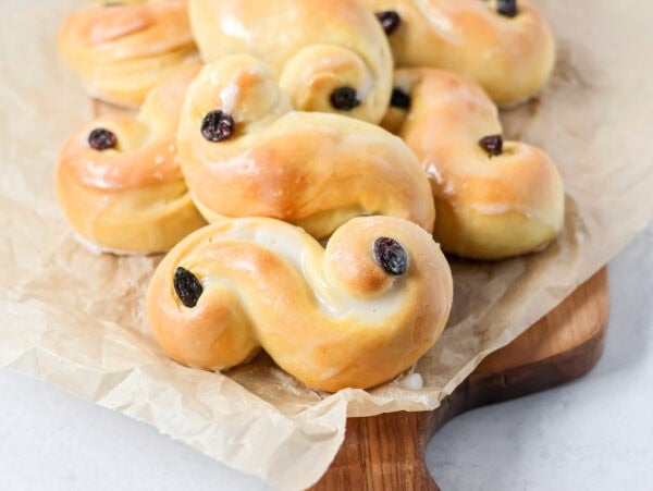 Baked and glazed St. Lucia Buns on a wooden cutting board.