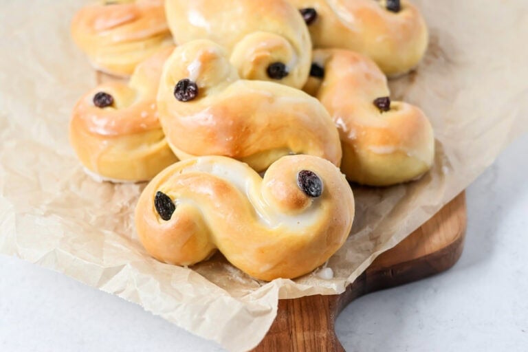 Baked and glazed St. Lucia Buns on a wooden cutting board.