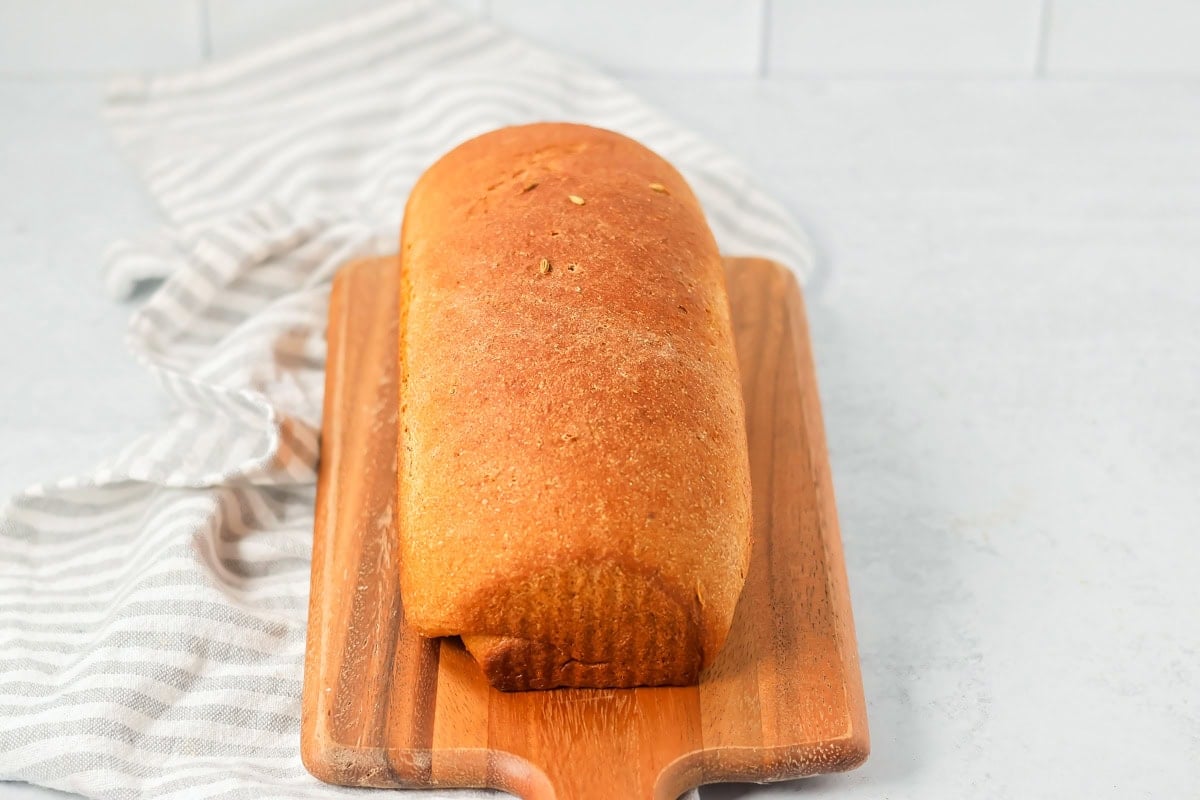 A loaf of baked limpa bread on a wooden cutting board.