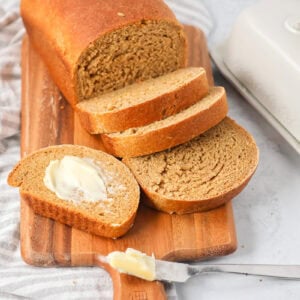 A loaf of sliced and buttered Swedish limpa bread on a wooden cutting board.