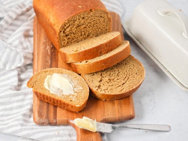 A loaf of sliced and buttered Swedish limpa bread on a wooden cutting board.