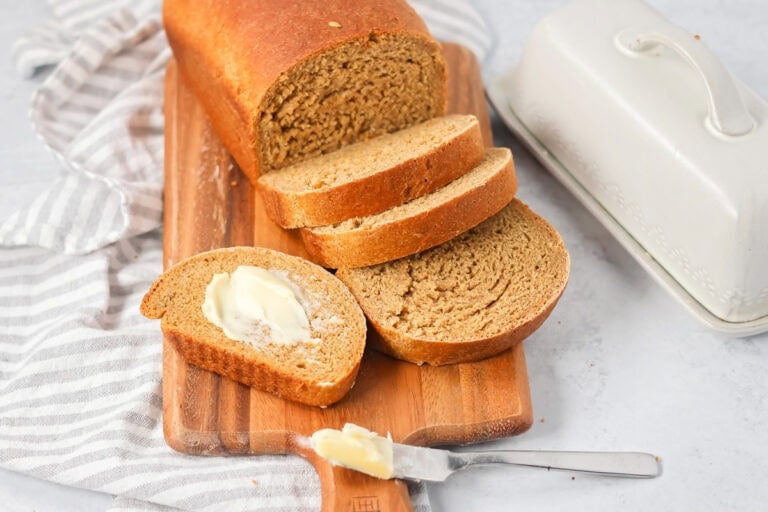 A loaf of sliced and buttered Swedish limpa bread on a wooden cutting board.