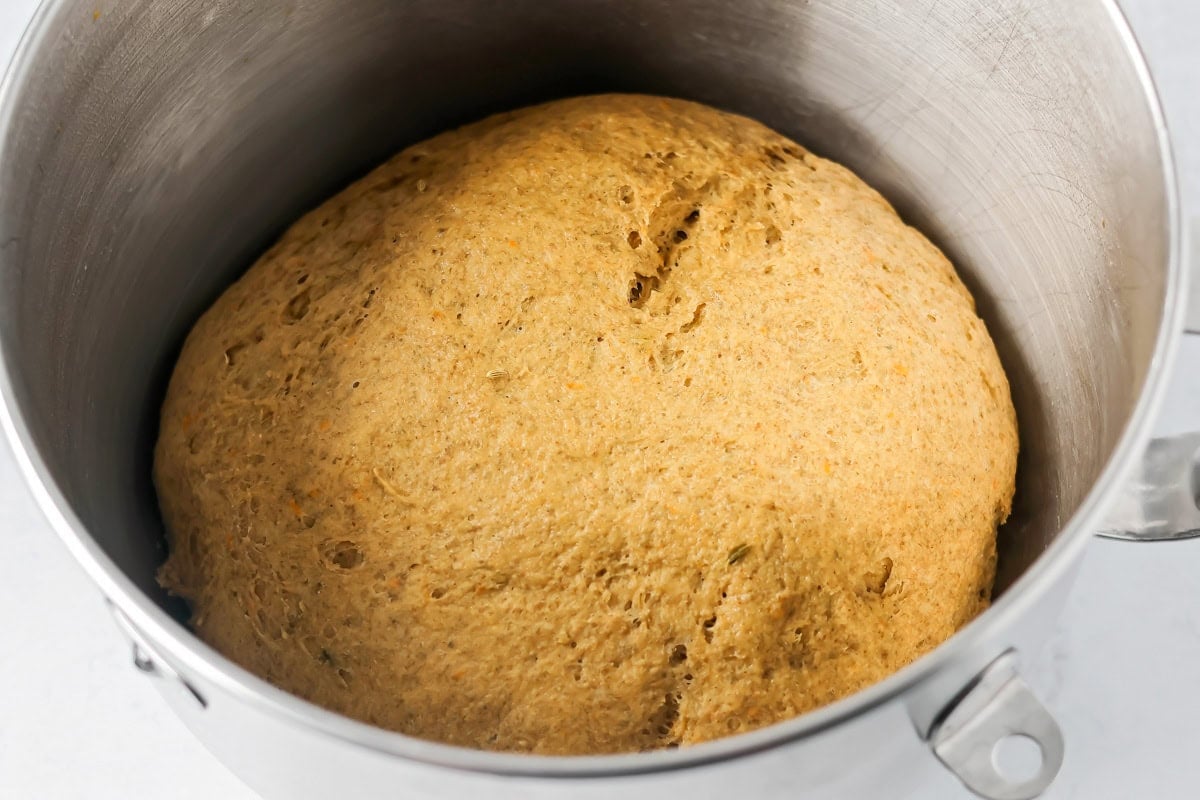 Swedish limpa bread dough rising in a metal bowl.