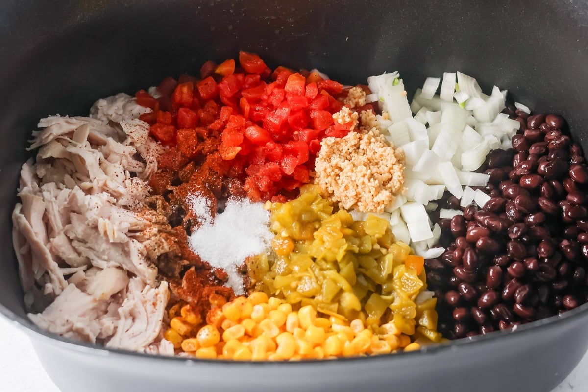 Adding turkey tortilla soup ingredients to a crock pot.